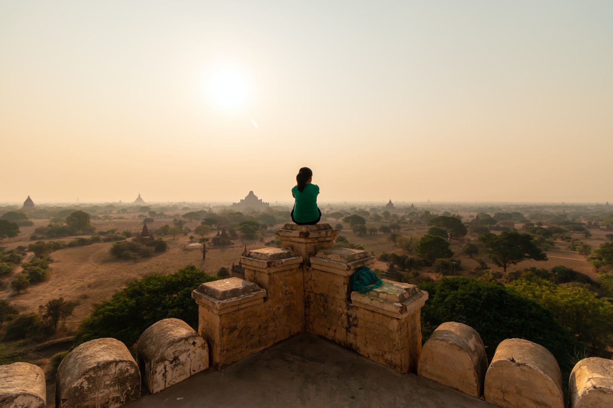 Traveler sitting atop a temple overlooking ancient Bagan at sunrise