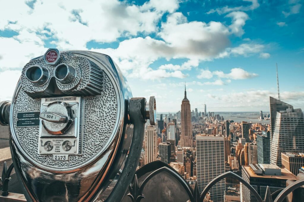 View of New York City skyline featuring iconic Empire State Building with observation binoculars in the foreground.