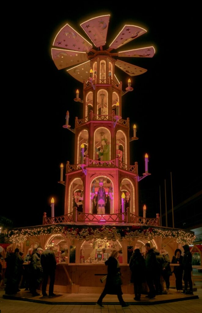 A christmas pyramid at night with people nearby.