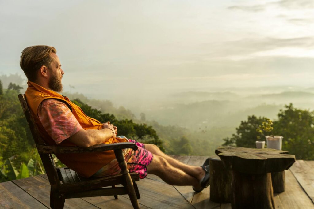 Man relaxing on a deck overlooking a misty mountain landscape at sunrise.