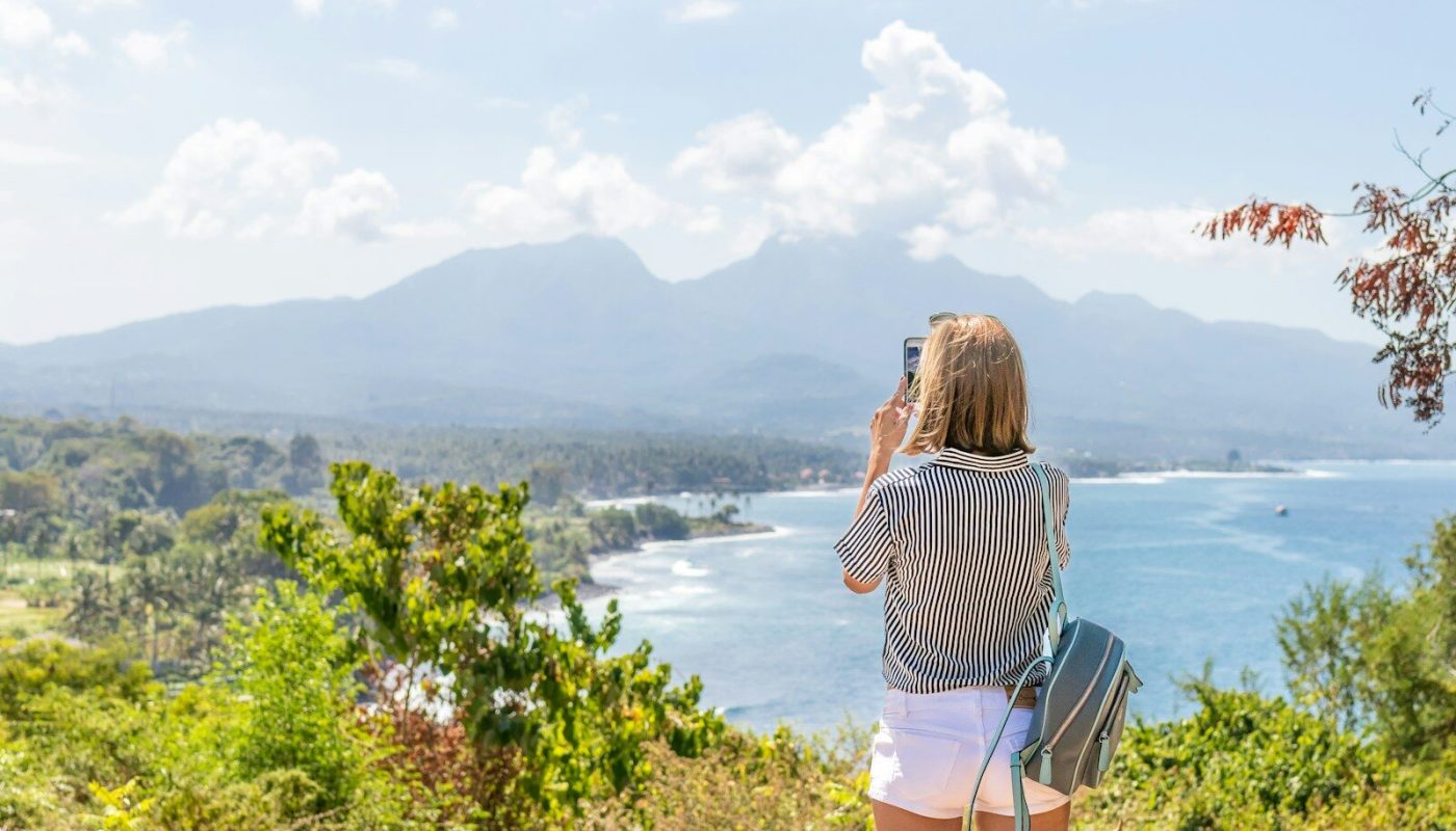 a woman taking a picture of the ocean with her cell phone